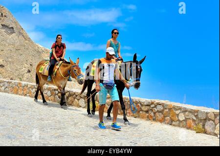 Zwei weibliche Touristen Esel reiten hinunter die Straße von antiken Thira, der Badeort von Kamari, Santorini, Griechenland Stockfoto