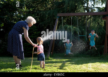 Familie mit Wasserschlauch im Sommer im Garten spielen. Stockfoto