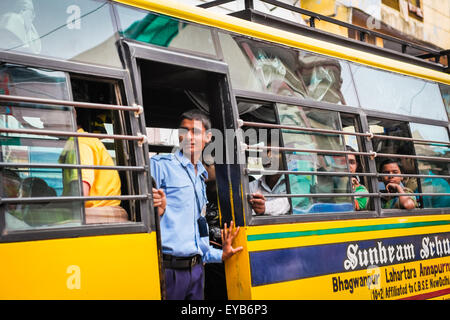 Ein Student, der aus der Eingangstür eines Schulbusses schaut, der sich auf einer belebten Straße in Varanasi, Uttar Pradesh, Indien, bewegt. Stockfoto