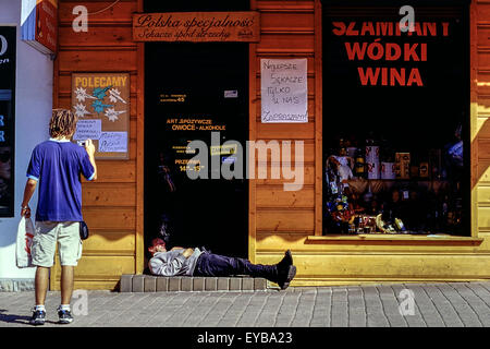 Ein Fußgänger fotografiert von einem schlafenden Mann in der Tür ein Wodka-Geschäft. Zakopane. Polen. Stockfoto