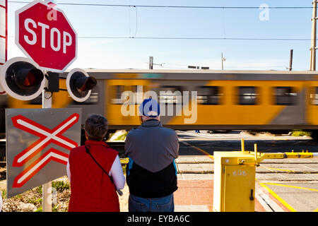 Ein paar Warten an einem Bahnübergang in Kalk Bay, Cape Provinz, Südafrika Stockfoto