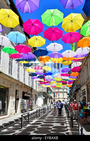 Blauer Himmel und Regenschirmfarben in der Street Art-Ausstellung in der antiken Stadt Arles Frankreich Provence werfen sich wiederholende Schattenmuster auf französische Einkaufsstraße Stockfoto