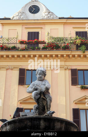 Cherub auf einen Brunnen mit einem Pastell farbigen Gebäude im Hintergrund. Stockfoto