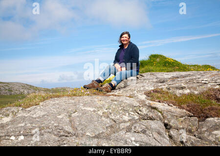 Applying weibliche Wanderer sitzen hoch auf Felsvorsprung in Barra, äußeren Hebriden, Schottland, Großbritannien Stockfoto