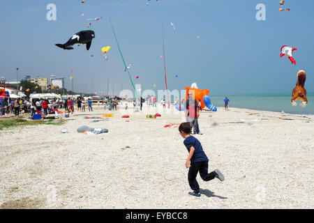 Ein kleiner Junge am Strand, bunte und Tier geformt Drachen fliegen über einem Strand. Stockfoto