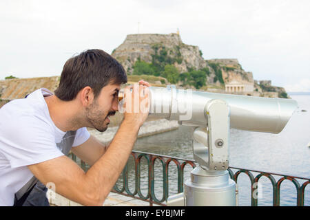 Junge Touristen Mann auf der Suche durch das öffentliche Fernglas an einem bewölkten Tag Stockfoto