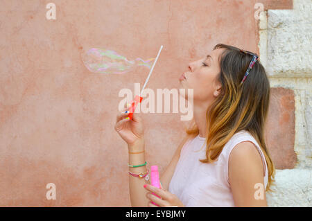 Mädchen bläst Seifenblasen vor bunten Hintergrund rosa Kleid Stockfoto