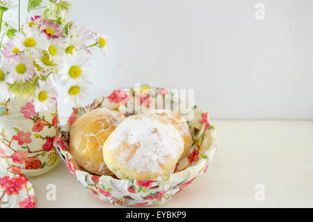 Hausgemachte Krapfen, bestreut mit Puderzucker in einer Serviettentechnik verziert Schale mit Blumen auf dem Tisch Stockfoto