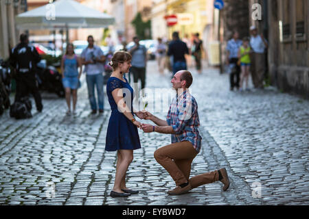 Paar in der Liebe auf der Straße. Mann auf die Knie gibt einer Frau eine Blume, ein Angebot macht. Mann und Frau während der Flitterwochen. Stockfoto