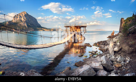 Schönen Sommer Sonnenuntergang am Meer mit Brückenbau, Berge und Steinen auf der Krim Stockfoto