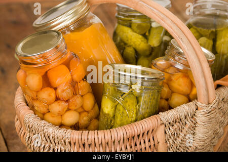 Startseite-Dosen produzieren (Rainier Kirschen, Butternut-Kürbis-Suppe und Dill Pickles) in einem großen Weidenkorb auf einem rustikalen Holztisch Stockfoto