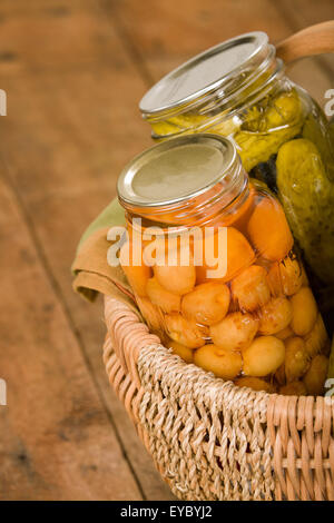 Startseite-Dosen produzieren (Rainier Kirschen und Dill Pickles) in einem großen Weidenkorb ruht auf einem rustikalen Holztisch Stockfoto