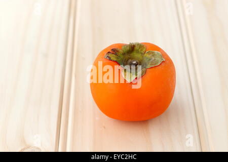 Ein frisches orange Farbe Kaki auf einem Holzbrett Stockfoto