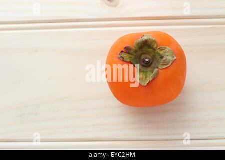 Ein frisches orange Farbe Kaki auf einem Holzbrett Stockfoto