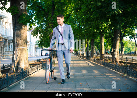 Gut aussehend Geschäftsmann zu Fuß mit dem Fahrrad auf der Straße in der Stadt Stockfoto