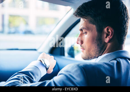 Gut aussehend Geschäftsmann auf Armbanduhr im Auto Stockfoto