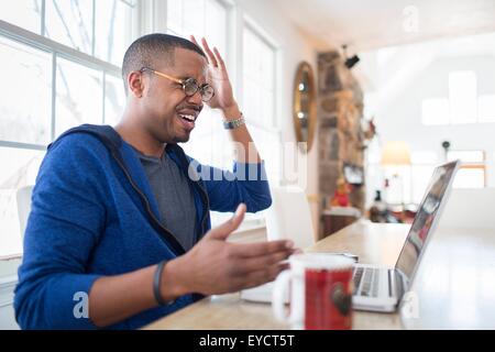 Mitte erwachsenen Mann mit Handzeichen ungläubig mit Laptop am Küchentisch Stockfoto