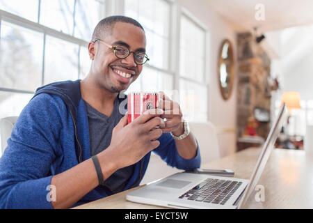Porträt von Mitte erwachsener Mann mit Laptop am Küchentisch Stockfoto