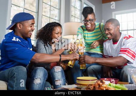 Vier Erwachsenen Freunden Toasten mit Flaschenbier auf Sofa im Wohnzimmer Stockfoto