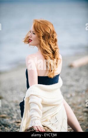 Junge Frau mit langen roten Haaren, die auf der Suche über die Schulter auf Strand, Bainbridge Island, Washington State, USA Stockfoto