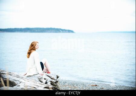 Junge Frau sitzt am Strand mit Blick auf Meer, Bainbridge Island, Washington State, USA Stockfoto