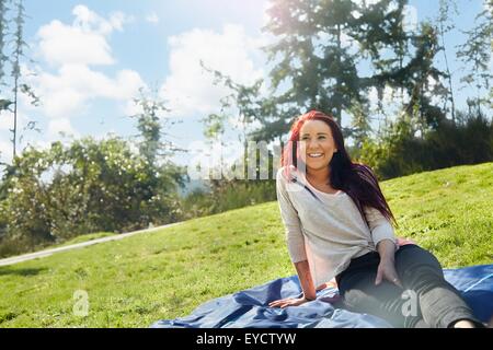 Junge Frau sitzt auf der Picknickdecke im park Stockfoto