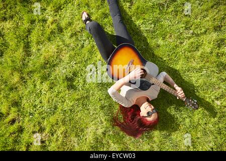 Draufsicht der jungen Frau liegt auf dem Rasen spielt akustische Gitarre Stockfoto