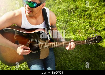 Junger Mann sitzt auf dem Rasen spielt akustische Gitarre Stockfoto