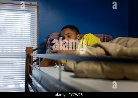 Teenager im Etagenbett Smartphone Text lesen liegend Stockfoto