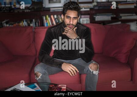 Junger Mann auf Sofa sitzend mit Hand am Kinn Stockfoto