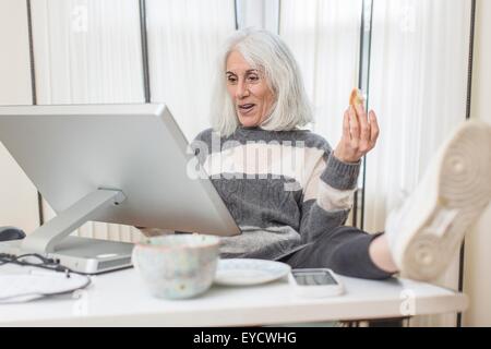 Porträt von senior Frau sitzt am Computer mit Fuß auf Schreibtisch Stockfoto