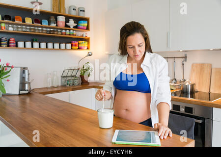 Schwangere Frau isst Joghurt mit tablet Stockfoto