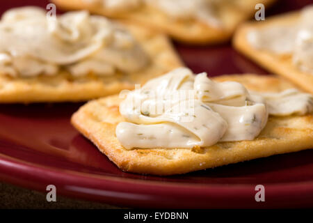 Nahaufnahme von Cracker mit Frischkäse auf einer roten Platte Stockfoto