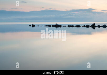 Wellenbrecher-Felsen im Meer der Ruhe mit Wolken und Spiegelungen im Wasser. Stockfoto