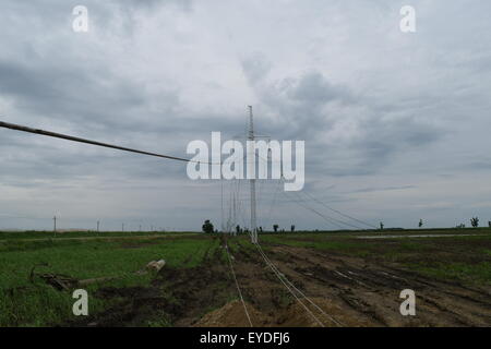 Hochspannungsleitungen und Strommasten in eine flache und grüne Agrarlandschaft an einem sonnigen Tag mit Cirruswolken am blauen Himmel Stockfoto