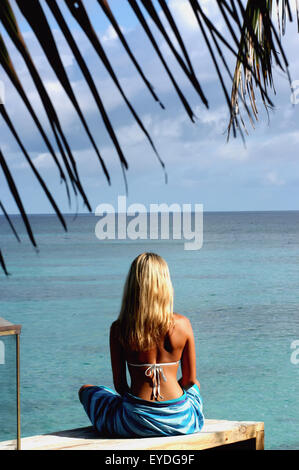 Frau im Sarong über Suche Meer im North Island Resort, North Island Seychellen auf Sonnendeck sitzen. Stockfoto