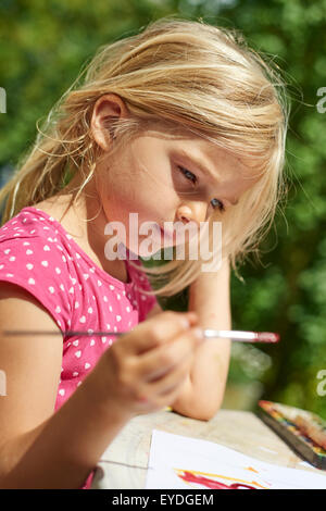 Ein Mädchen, Malen mit Wasserfarben (Aquarelle), malt ein Pappteller mit Aquarell Malen draußen im Garten Stockfoto