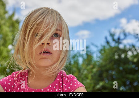 Porträt von erstaunt, überrascht und schockiert Kind blondes Mädchen draußen, Sommer, Garten, Park, Garten, Bäume Hintergrund Stockfoto
