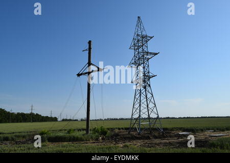 Hochspannungsleitungen und Strommasten in eine flache und grüne Agrarlandschaft an einem sonnigen Tag mit Cirruswolken am blauen Himmel Stockfoto