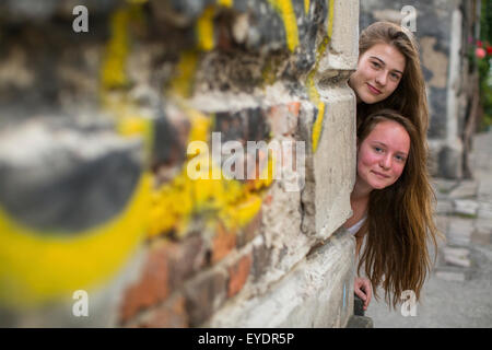 Zwei süße Teenie Mädchen blicken hinter die Ecke eines Steinhauses. Stockfoto