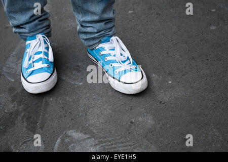 Blaue Turnschuhe stehen Teenager Füße in Detektive auf dunklen grauen Asphalt. Nahaufnahme Foto mit Tiefenschärfe und flachen DOF Stockfoto