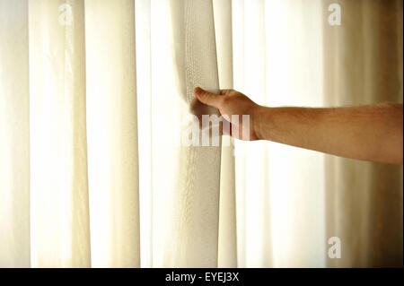 Die Hand eines Mannes ziehen ein Fenstervorhang für warme Tageslicht in den Raum zu betreten Stockfoto