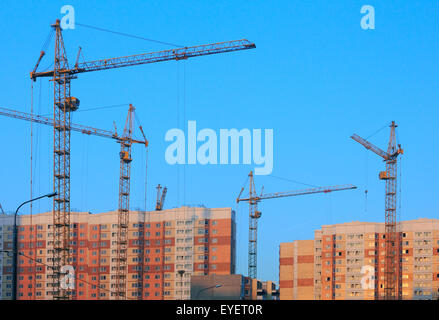 Krane auf der Baustelle des neuen Wohnblocks bei Sonnenuntergang. Stockfoto