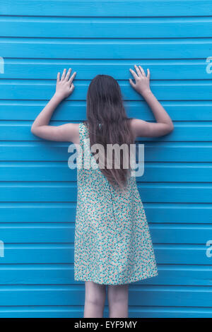 eine Mädchen mit einem geblümten Kleid ist an einer Holzwand gelehnt.