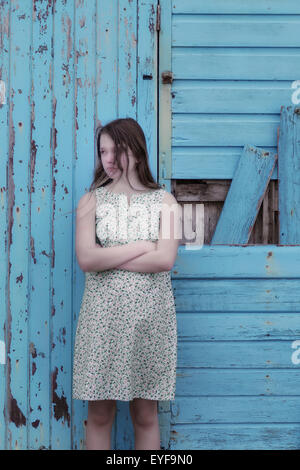 eine Mädchen in einem geblümten Kleid steht vor einer blauen Wand aus Holz