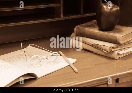 Altmodische Brille auf Notebook auf alten hölzernen Lehrerpult mit Apfel auf Bücherstapel getragen. Stockfoto