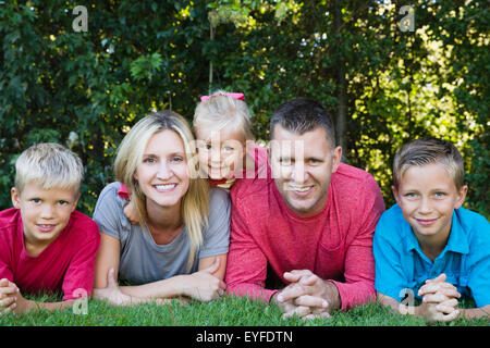Eltern mit Söhnen (8-9, 10-11) und Tochter (2-3) liegen auf dem Rasen Stockfoto