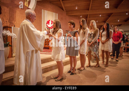 Ein Priester salbt eine Linie von Teen Girls bei Bestätigung Zeremonien in einer Laguna Niguel, CA, katholische Kirche.  Bestätigung ist eines der sieben Sakramente, die Katholiken in den Prozess der religiösen Erziehung durchlaufen. Hinweis vietnamesische amerikanische Priester. Stockfoto