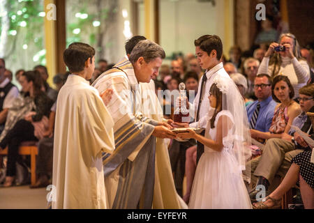 In formalen Outfits, multirassische Kinder bringen die Sakramente Wein und Gastgeber Wafer von Monsignore bei der Messe am Laguna Niguel, CA, katholische Kirche für Erstkommunion Zeremonien gesegnet werden. Stockfoto