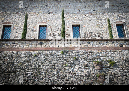 Steinmauer einer mittelalterlichen Festung mit vier Fenstern und einem kleinen hängenden Garten. Stockfoto